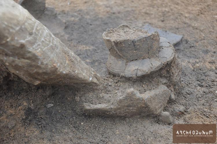 Détail du dépôt funéraire de l’âge du Bronze : gobelet et fond de vase en céramique avec une pierre basculée.